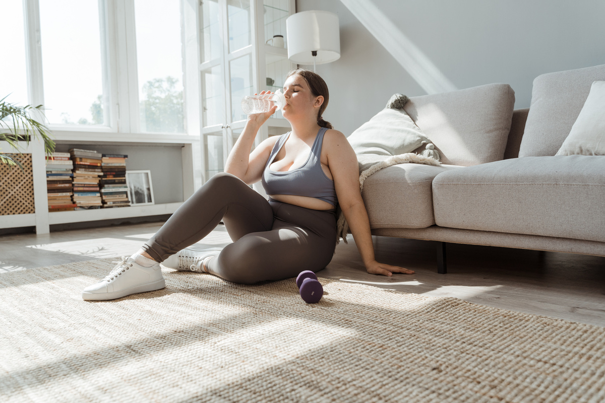 A Tired Woman Sitting on the Carpeted Flooring while Drinking Water